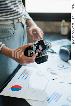 A person holding a vintage camera while reviewing business reports, blending creativity with strategic planning in a modern office. 124369997