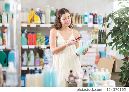 Young girl in summer clothes scanning QR-code on cleaning spray in store 124370165