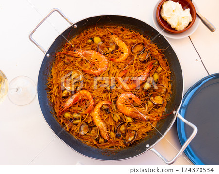 Seafood fideua with shrimps, squid and clams in paellera with allioli 124370534