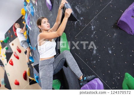 Young girl moving on bouldering wall at indoor climbing gym Young girl moving on bouldering wall at indoor climbing gym 124370572