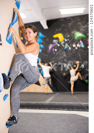 Young woman climbs steep artificial wall in sports complex and trains endurance 124370601