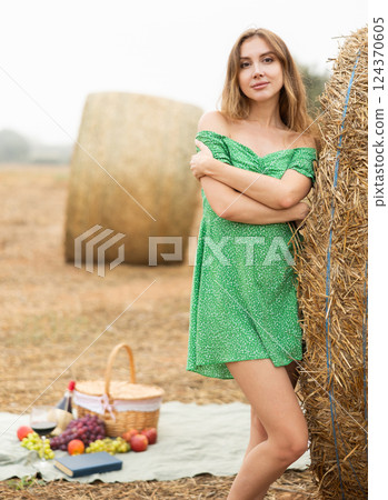 Young seductive sexy girl in summer green dress posing near stack of straw enjoying holidays in countryside in field 124370605