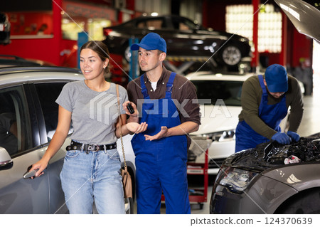 Kind car mechanic handing over the keys of car to glad female client in auto shop Kind car mechanic handing over the keys of car to glad female client in auto shop 124370639