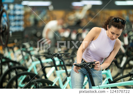 Attentive woman examining quality seat and choosing bike in bicycle sports store 124370722