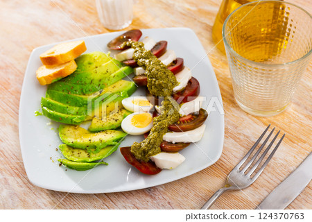 Slices of mozzarella and tomatoes - Italian salad caprese with addition boiled eggs and avocado Slices of mozzarella and tomatoes - Italian salad caprese with addition boiled eggs and avocado 124370763