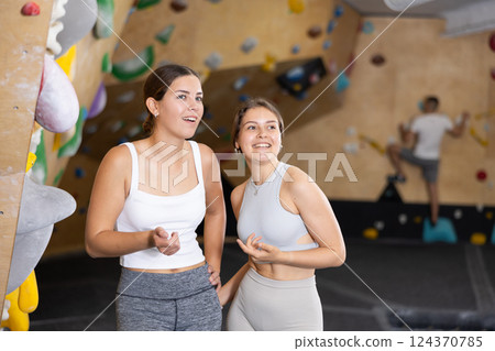Young women are standing in gym and discussing possible options for overcoming difficult climbing route 124370785
