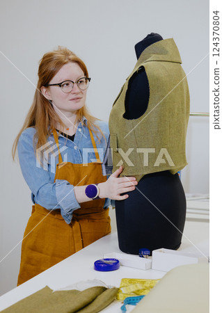 female fashion designer seamstress with red hair tries on clothes for a mannequin.  124370804