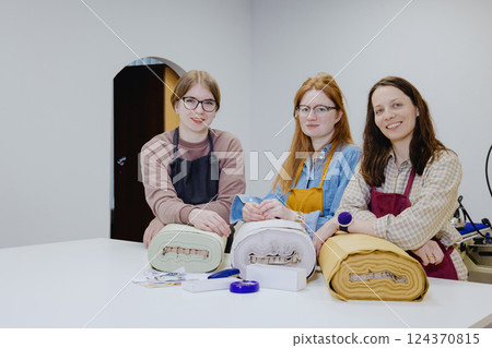 Three female seamstresses and fashion designers are standing at a table with a roll of fabric Three female seamstresses and fashion designers are standing at a table with a roll of fabric 124370815