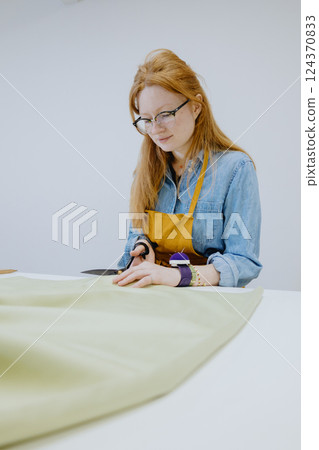 female seamstress cuts product from a roll of fabric in sewing workshop. fashion industry. 124370833
