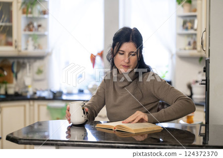 Cozy moments of reflection and learning over a warm drink in a sunlit kitchen while exploring the pages of a captivating book 124372370