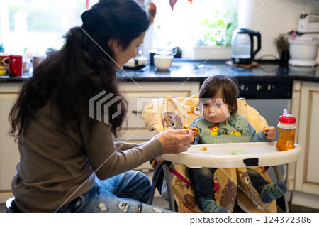 Little one's lunchtime adventure unfolds in a cozy kitchen, mama sharing food, creating memories, a sweet bond, as baby explores new flavors, learning and growing with every bite 124372386