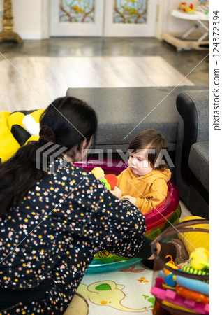 Indoor playtime unfolds in a cozy room as a caring woman engages with a baby seated in an inflatable pool with colorful toys, creating a heartwarming family moment Indoor playtime unfolds in a cozy room as a caring woman engages with a baby seated in an inflatable pool with colorful toys, creating a heartwarming family moment 124372394