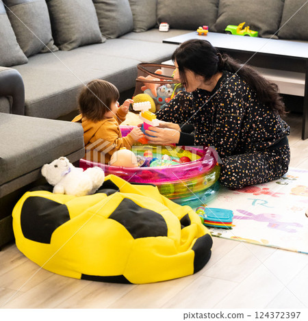 Playful afternoon in a cozy living room with a cheerful child enjoying colorful toys and engaging with a caring adult Playful afternoon in a cozy living room with a cheerful child enjoying colorful toys and engaging with a caring adult 124372397