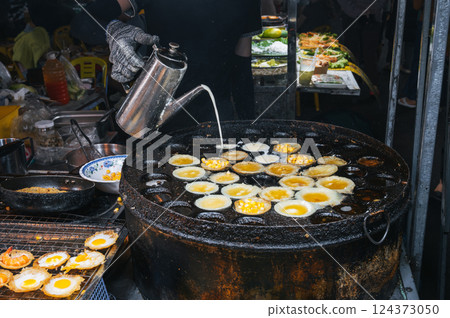 cooking a traditional Vietnamese dish Banh Khot with shrimps and corn at Asian night market on street in Vietnam in Asia cooking a traditional Vietnamese dish Banh Khot with shrimps and corn at Asian night market on street in Vietnam in Asia 124373050