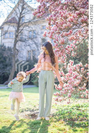 Young mother with her little daughter in a blooming magnolia garden in Prague. Symbol of maternal love and the beauty of springtime bonding in nature 124373082