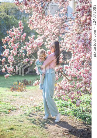 Trendy mom with her little daughter under blooming magnolia trees in a Prague park. Capturing a stylish family moment with a modern approach to parenting 124373085