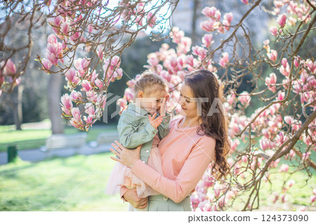 Trendy mom with her little daughter under blooming magnolia trees in a Prague park. Capturing a stylish family moment with a modern approach to parenting 124373090