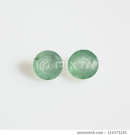 Close-up of Two Faceted Natural Emerald Gemstones Against a Clean White Background, Showcasing Their Green Hue and Internal Inclusions 124373285
