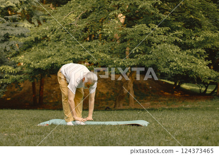 Senior man in white t-shirt standing at park and doing excercises. Positive mature woman has fitness or yoga class in nature. Wellness and healthy lifestyle on retirement. 124373465