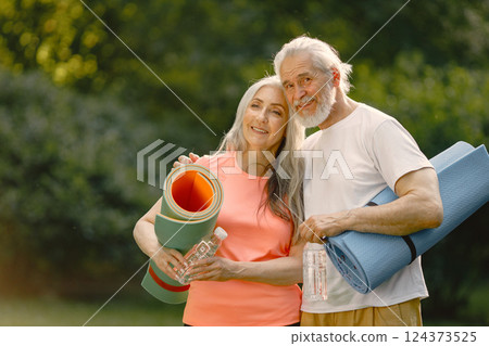 Senior man and woman with yoga mats standing at park. Positive mature man and his elderly wife after fitness or yoga class in nature. Wellness and healthy lifestyle on retirement. Senior man and woman with yoga mats standing at park. Positive mature man and his elderly wife after fitness or yoga class in nature. Wellness and healthy lifestyle on retirement. 124373525