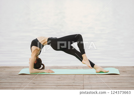 Pretty lady training in a summer park. Brunette doing yoga. Girl in a sportsuit. Pretty lady training in a summer park. Brunette doing yoga. Girl in a sportsuit. 124373663