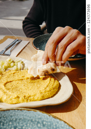 man dips a piece of naan bread on hummus man dips a piece of naan bread on hummus 124373696