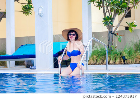 Relaxing by the pool: Woman in bikini and hat enjoying warm water in luxury Dubai hotel enjoying sun and peace, luxury holiday concept Relaxing by the pool: Woman in bikini and hat enjoying warm water in luxury Dubai hotel enjoying sun and peace, luxury holiday concept 124373917