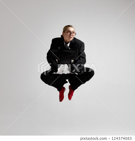 Businesswoman mid-motion with briefcase in hand, leaping in lotus pose with frightened expression. Concept of professional urgency. 124374083