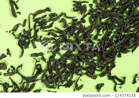 Unbrewed black tea scattered on bright green backdrop 124374138