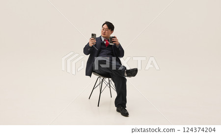Coffee break. Young Asian man browsing on phone and drinking coffee having rest time against white background. Coffee break. Young Asian man browsing on phone and drinking coffee having rest time against white background. 124374204