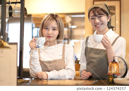Two female baristas holding coffee cups at the counter 124374257