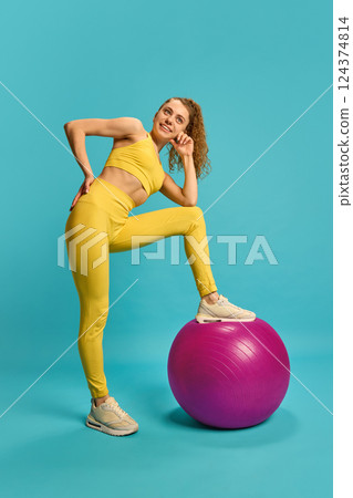 Fit woman standing with leg on stability ball, smiling in confident pose, showing motivation and readiness for training. 124374814