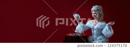Confident winner. Stylish rococo woman with cards and chips, posing like casino queen in white baroque gown. 124375178