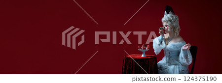 Waiting act. Lady in rococo costume playfully holding opera glasses, looking at pomegranate against red background. 124375190