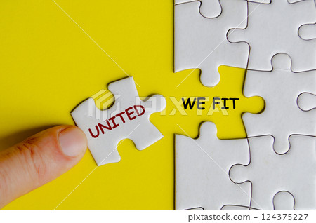 Hand placing missing jigsaw puzzle with text United We Fit representing teamwork and unity. Teamwork concept 124375227
