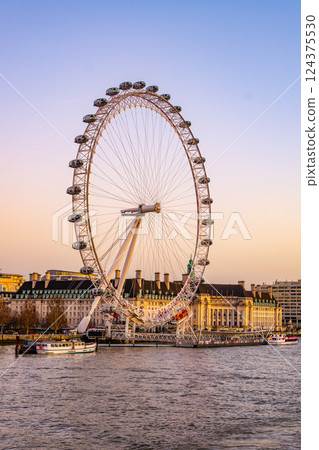 Towering over the South Bank, the London Eye offers a breathtaking view of the city. Boats gently glide along the River Thames as dusk settles, creating a picturesque setting. Towering over the South Bank, the London Eye offers a breathtaking view of the city. Boats gently glide along the River Thames as dusk settles, creating a picturesque setting. 124375530