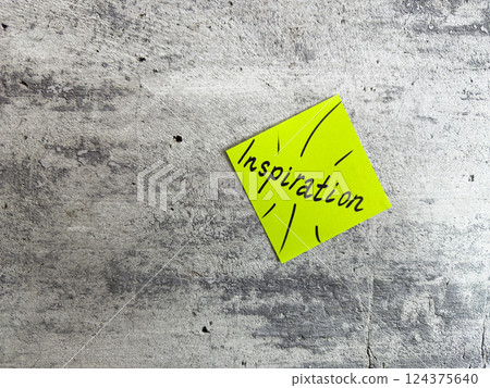 Bright yellow sticky note shaped as a diamond featuring the word Inspiration and decorative elements on a textured grey background, symbolizing the power of motivating ideas and creativity 124375640