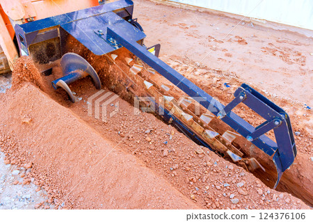 Trencher machinery is actively digging into earth at construction site Trencher machinery is actively digging into earth at construction site 124376106