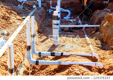 Plumber are engaged in placing wastewater piping in trench during work day at construction site. 124376107