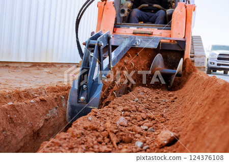 Trencher cuts through soil as worker prepare for underground utility installation in construction area 124376108