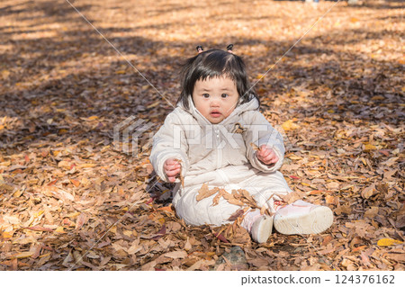 [一名 1 歲的孩子坐在覆蓋著落葉的冬季公園裡玩耍] 124376162