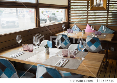 Cozy modern restaurant interior with wooden tables and geometric chairs by large windows 124376740