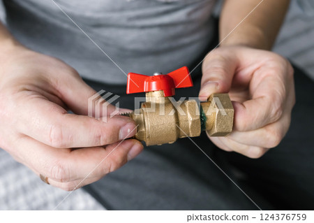 Hands assembling brass valve with red handle indoors 124376759