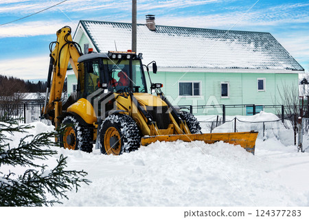 Yellow backhoe loader is clearing snow, machine front blade is pushing snowdrift. 124377283