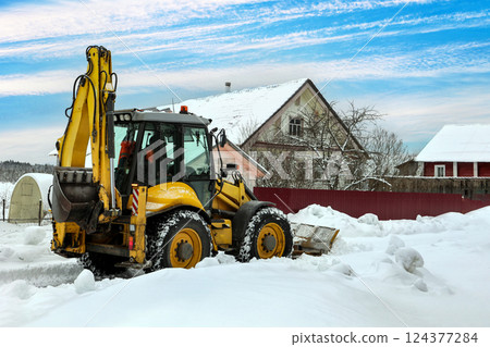 Articulated backhoe loader uses hydraulics to drive dozer blade for snow removal, while high-traction tires ensure maneuverability across snow covered terrain near buildings. Articulated backhoe loader uses hydraulics to drive dozer blade for snow removal, while high-traction tires ensure maneuverability across snow covered terrain near buildings. 124377284