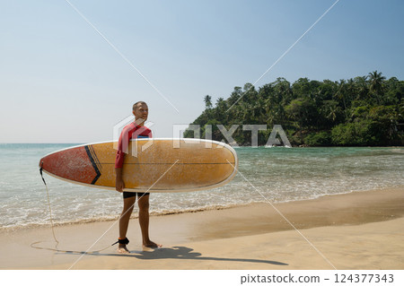 Young handsome man surfer going to surfing. Outdoors. Hiriketiya Beach, Dikwella. Sri Lanka. Tropical coastline. Young handsome man surfer going to surfing. Outdoors. Hiriketiya Beach, Dikwella. Sri Lanka. Tropical coastline. 124377343