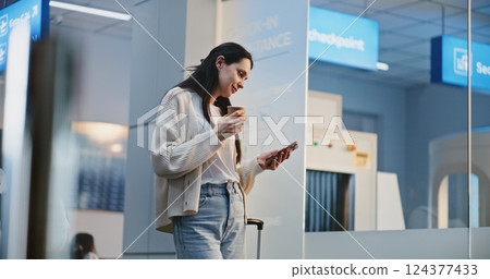 Busy Airport Terminal: Adult Woman Scrolling on Smartphone, Drinking Coffee, Waiting for Flight 124377433