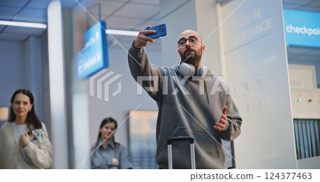 Crowded Airport Terminal: Tourist Talking on Phone by Video Call or Recording Video Content 124377463