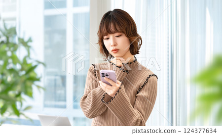 女人/女商人一邊看著智慧型手機一邊思考 女人/女商人一邊看著智慧型手機一邊思考 124377634