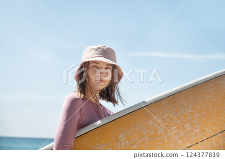 Portrait of young woman surfer going to surfing. Her face is protected by natural spf surf zinc. Surfing of woman at beach with surfboard for freedom. Travel outdoor. Portrait of young woman surfer going to surfing. Her face is protected by natural spf surf zinc. Surfing of woman at beach with surfboard for freedom. Travel outdoor. 124377839